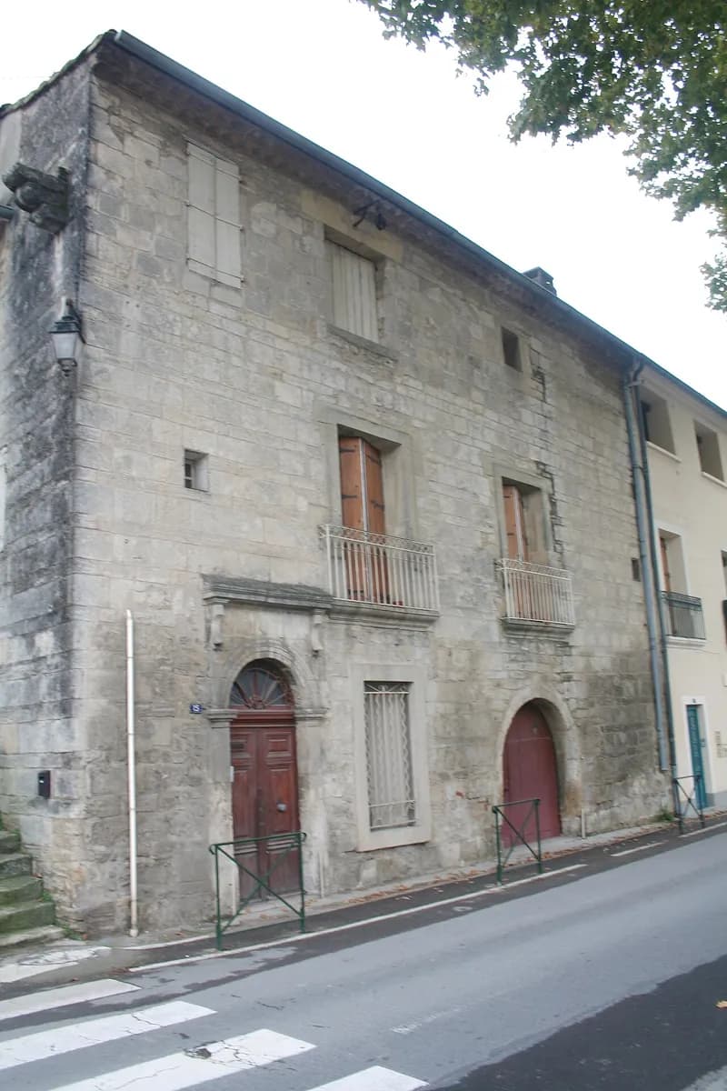 Façade d'une vieille maison en pierre de taille à Lavérune, porte en arc et balcons en fer forgé, au bord de la rue