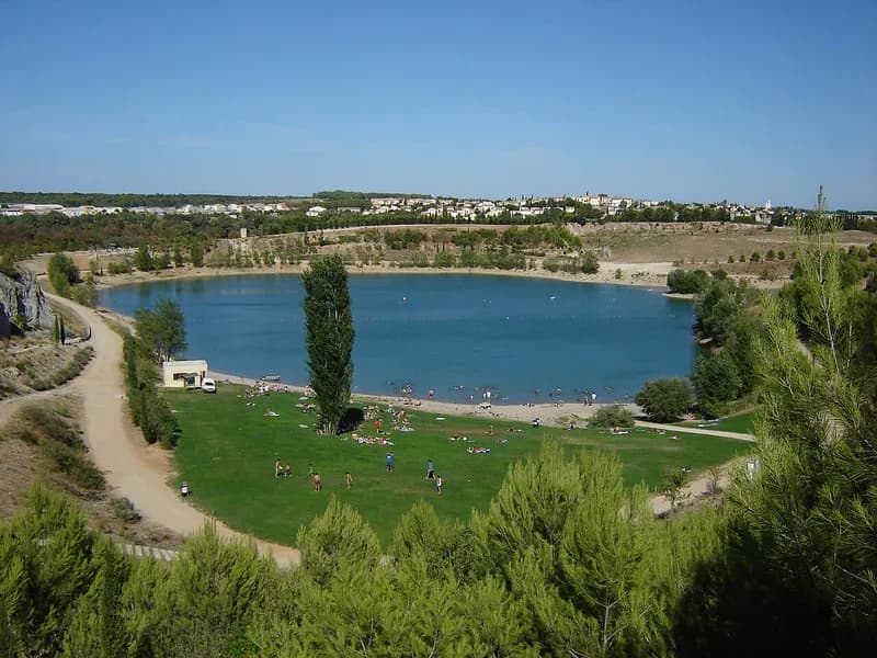 Le lac du Crès vu depuis les pins qui le dominent, avec sa pelouse de baignade et les maisons de la commune à l'horizon