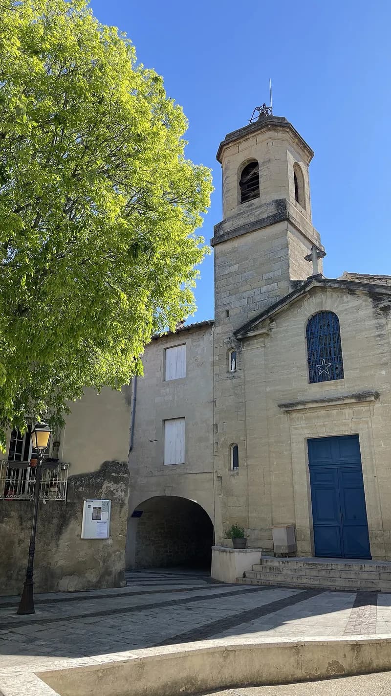 Façade et clocher en pierre de l'église Saint-Jean-Baptiste de Saint-Jean-de-Védas, porte bleue et passage voûté